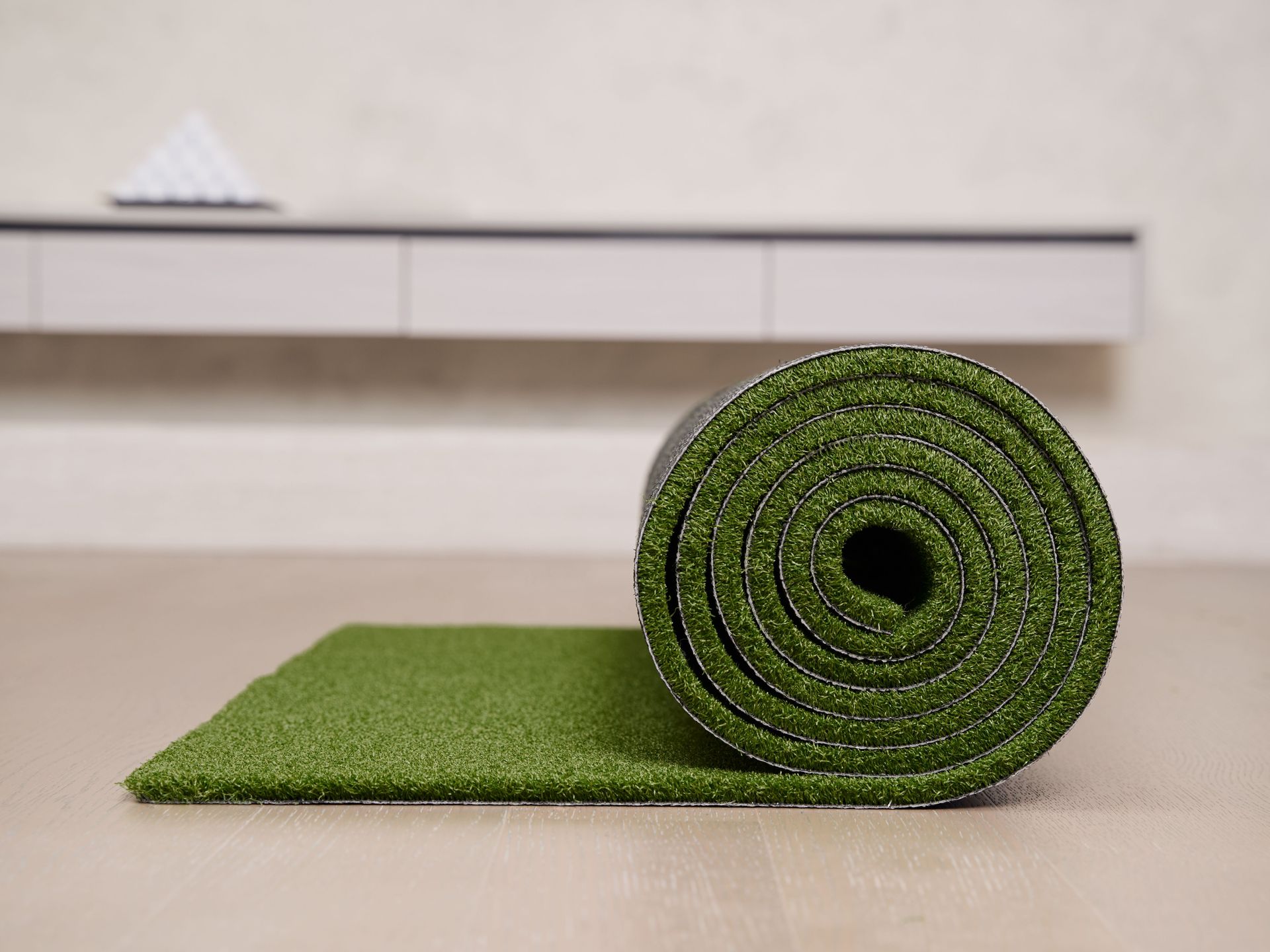 Close-up of a rolled artificial turf mat on a floor, ideal for indoor golf practice.