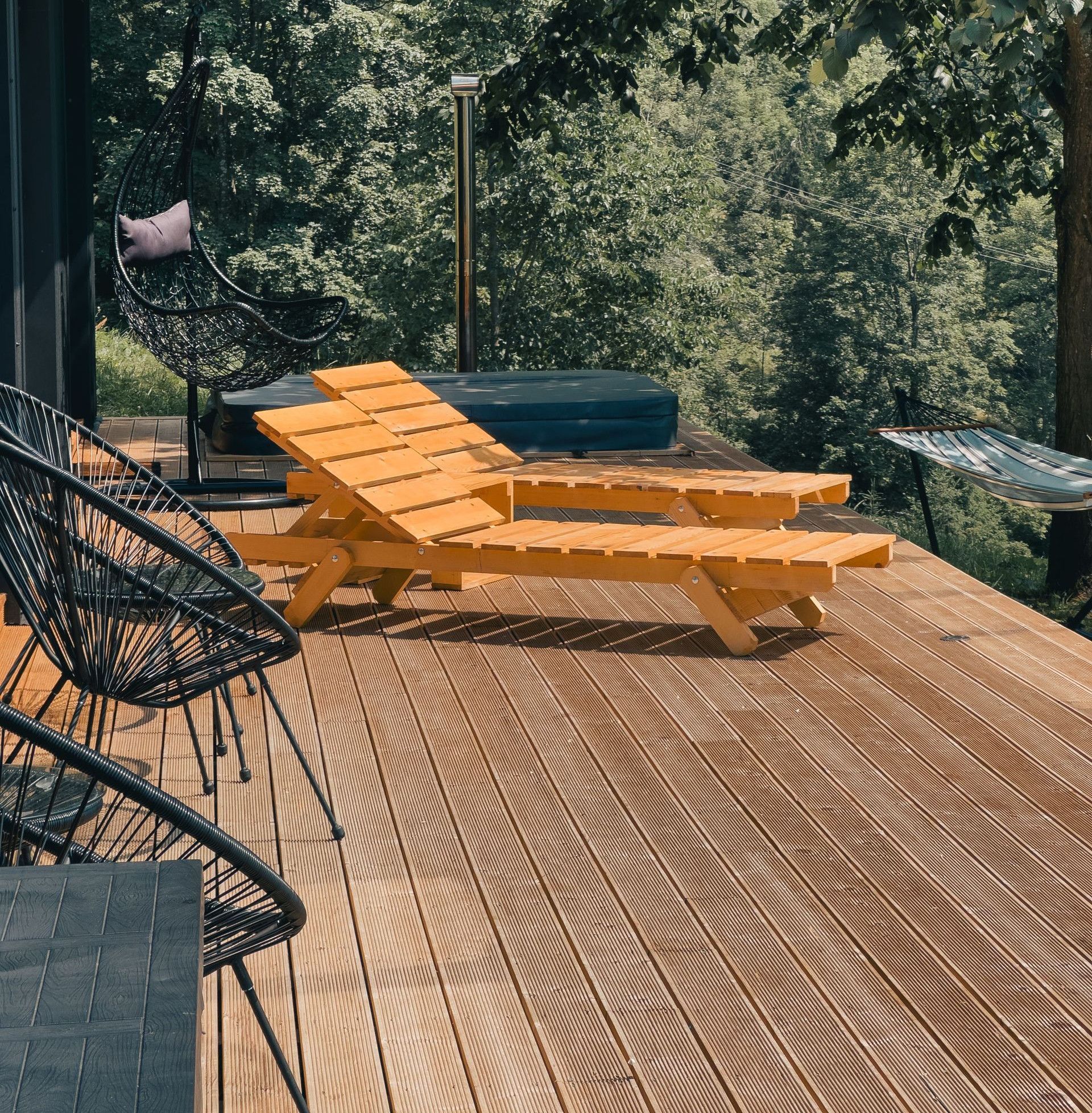 Wooden deck with lounge chairs surrounded by lush greenery, perfect for relaxation.