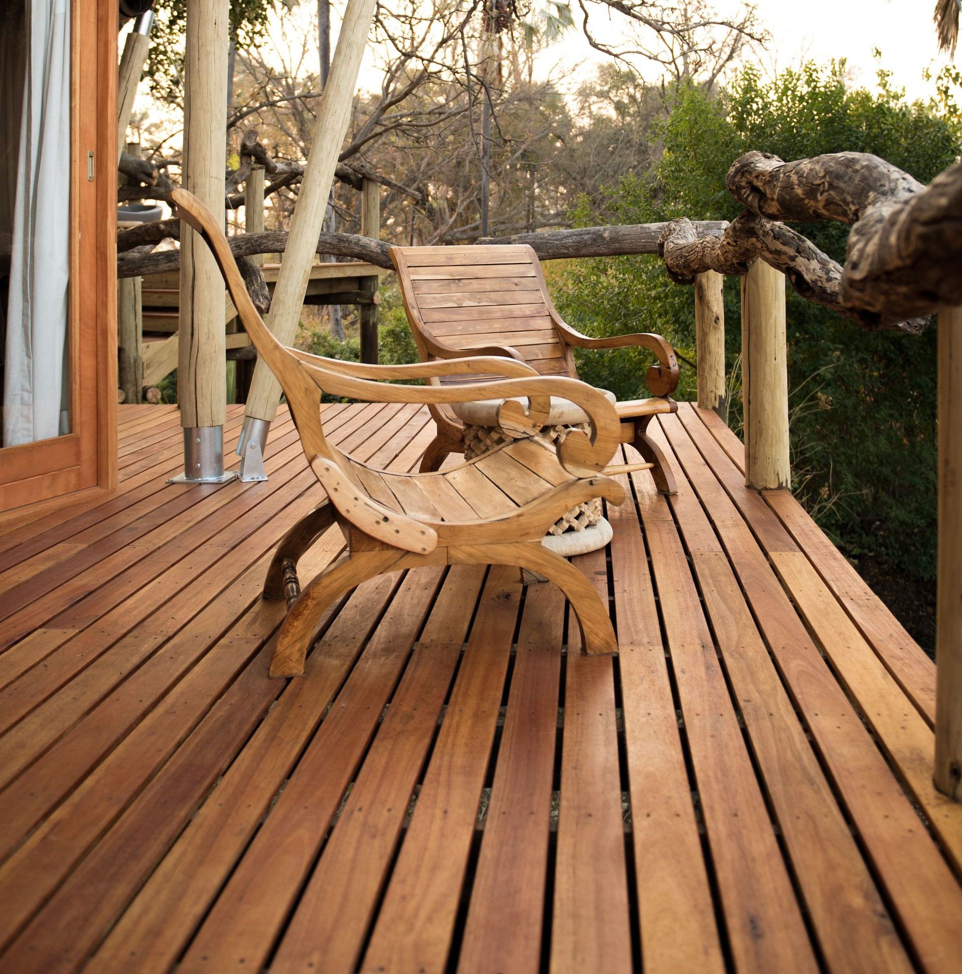 Two wooden chairs on a rustic deck surrounded by lush nature.